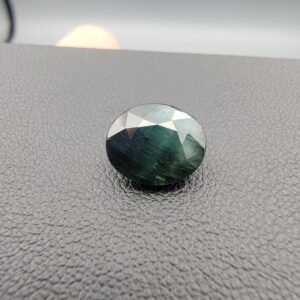A 4.28-carat natural sapphire from Kanchanaburi, Thailand, displaying a unique bi-color blue and green blend in an oval faceted cut, presented in a white jeweler's box.
