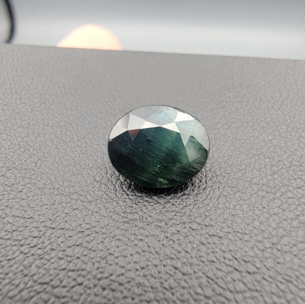 A 4.28-carat natural sapphire from Kanchanaburi, Thailand, displaying a unique bi-color blue and green blend in an oval faceted cut, presented in a white jeweler's box.