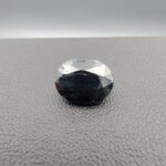 A 4.91-carat natural blue sapphire from Kanchanaburi, Thailand, in an oval faceted cut, featuring deep blue color and visible natural surface fissures, displayed in a white jeweler's box.