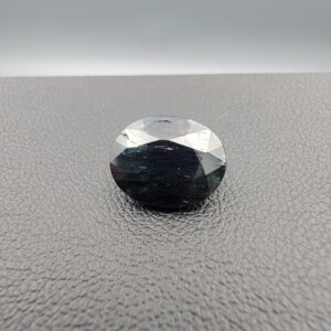 A 4.91-carat natural blue sapphire from Kanchanaburi, Thailand, in an oval faceted cut, featuring deep blue color and visible natural surface fissures, displayed in a white jeweler's box.