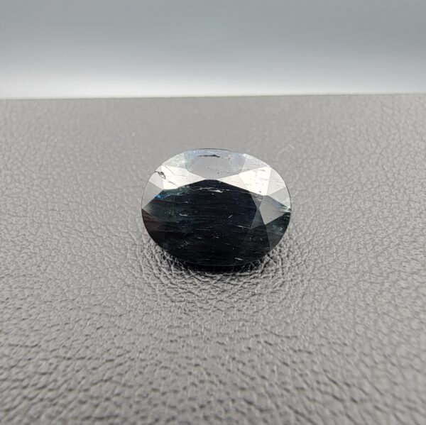 A 4.91-carat natural blue sapphire from Kanchanaburi, Thailand, in an oval faceted cut, featuring deep blue color and visible natural surface fissures, displayed in a white jeweler's box.