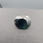 A 4.54-carat natural sapphire from Kanchanaburi, Thailand, showcasing a unique bi-color blue and green blend in a classic oval faceted cut, displayed in a white jeweler's box.