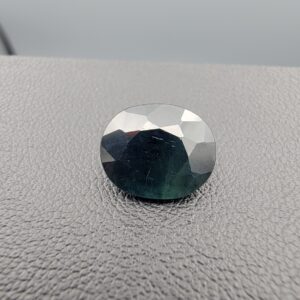 A 4.54-carat natural sapphire from Kanchanaburi, Thailand, showcasing a unique bi-color blue and green blend in a classic oval faceted cut, displayed in a white jeweler's box.