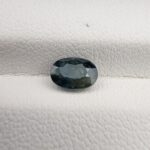 A 0.99-carat natural teal blue sapphire from Kanchanaburi, Thailand, with an oval faceted cut and a saturated blue-green color, presented in a professional jeweler's box