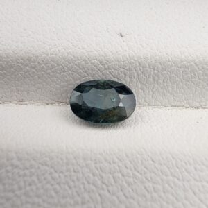 A 0.99-carat natural teal blue sapphire from Kanchanaburi, Thailand, with an oval faceted cut and a saturated blue-green color, presented in a professional jeweler's box
