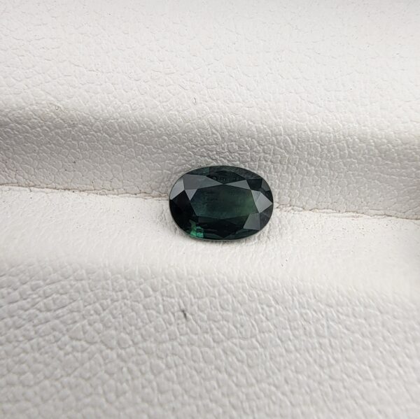 A 0.96-carat natural teal blue sapphire from Kanchanaburi, Thailand, featuring a classic oval faceted cut and a saturated blue-green color, presented in a professional white jeweler's box.