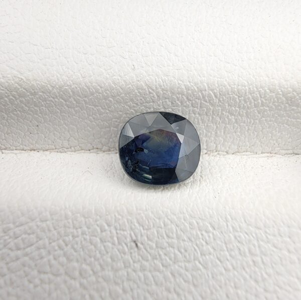 ​A 1.28-carat natural teal blue sapphire from Kanchanaburi, Thailand, with an oval faceted cut and a saturated blue-green color, presented in a professional white jeweler's box.