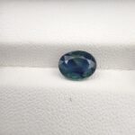 A large 2.06-carat natural teal blue sapphire from Kanchanaburi, Thailand, featuring a masterfully faceted oval cut and deep blue-green saturation, shown in a professional white jeweler's box.