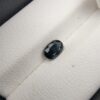 A 0.99-carat natural teal blue sapphire from Kanchanaburi, Thailand, with an oval faceted cut and a saturated blue-green color, presented in a professional jeweler's box.