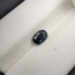 A 0.99-carat natural teal blue sapphire from Kanchanaburi, Thailand, with an oval faceted cut and a saturated blue-green color, presented in a professional jeweler's box.