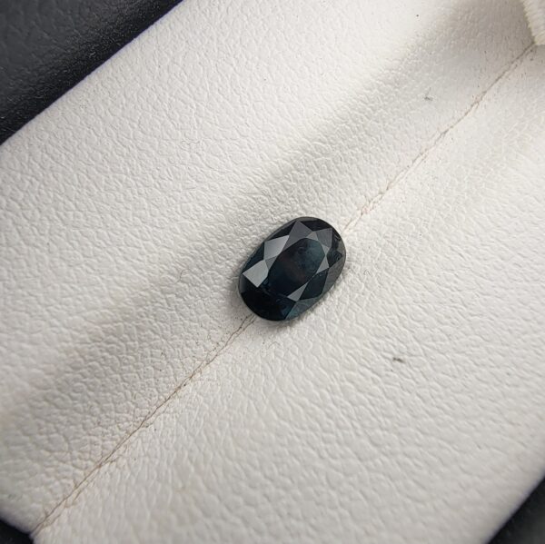A 0.99-carat natural teal blue sapphire from Kanchanaburi, Thailand, with an oval faceted cut and a saturated blue-green color, presented in a professional jeweler's box.