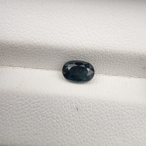 A 0.99-carat natural teal blue sapphire from Kanchanaburi, Thailand, with an oval faceted cut and a saturated blue-green color, presented in a professional jeweler's box.