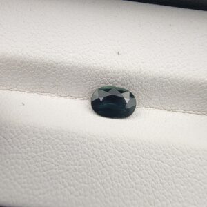 A 0.96-carat natural teal blue sapphire from Kanchanaburi, Thailand, featuring a masterfully faceted oval cut and deep blue-green saturation, presented in a professional white jeweler's box.