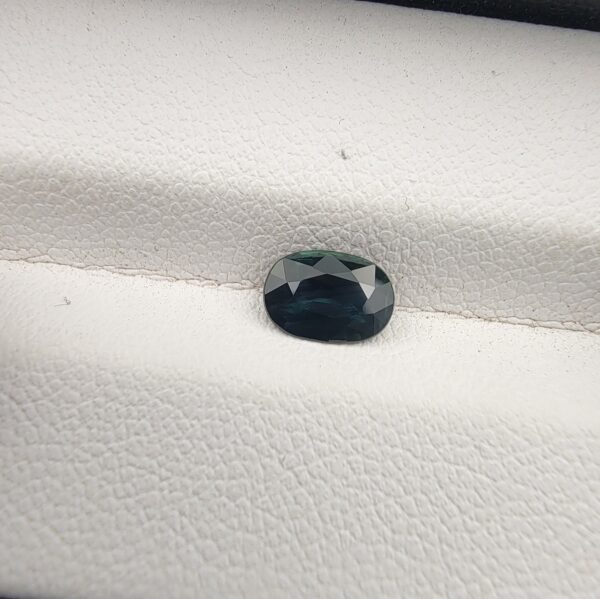 A 0.96-carat natural teal blue sapphire from Kanchanaburi, Thailand, featuring a masterfully faceted oval cut and deep blue-green saturation, presented in a professional white jeweler's box.