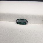 ​A 0.89-carat natural teal blue sapphire from Kanchanaburi, Thailand, featuring a classic oval faceted cut and saturated blue-green color, presented in a professional white jeweler's box.