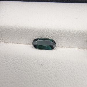 ​A 0.89-carat natural teal blue sapphire from Kanchanaburi, Thailand, featuring a classic oval faceted cut and saturated blue-green color, presented in a professional white jeweler's box.
