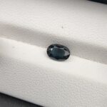 A 1.01-carat natural blue sapphire from Kanchanaburi, Thailand, featuring a masterfully faceted oval cut and deep royal blue color, presented in a professional white jeweler's box.