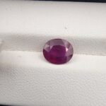A 2.30-carat natural Mozambique ruby with a purplish-red color and oval faceted cut, showing natural white inclusions on the inner surface, presented in a professional jeweler's box.