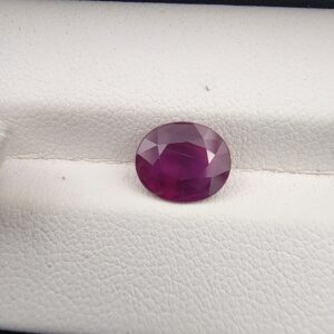 A 2.30-carat natural Mozambique ruby with a purplish-red color and oval faceted cut, showing natural white inclusions on the inner surface, presented in a professional jeweler's box.