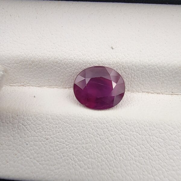 A 2.30-carat natural Mozambique ruby with a purplish-red color and oval faceted cut, showing natural white inclusions on the inner surface, presented in a professional jeweler's box.