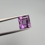 A natural 3.72-carat Brazilian amethyst (Katela) with a bright purple saturation and a sharp square faceted cut, held in professional jeweler's tweezers against a neutral background.