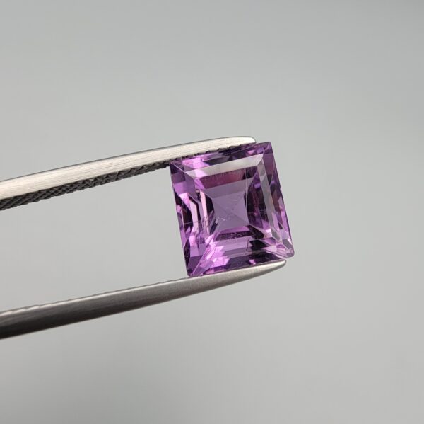 A natural 3.72-carat Brazilian amethyst (Katela) with a bright purple saturation and a sharp square faceted cut, held in professional jeweler's tweezers against a neutral background.