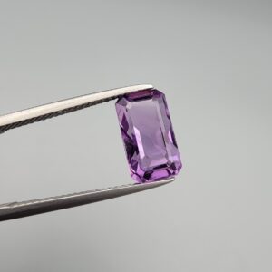 A natural 4.28-carat Brazilian amethyst (Katela) with a bright purple saturation and a sharp rectangle faceted cut, held in professional jeweler's tweezers.
