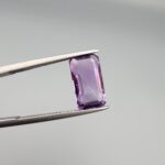 ​A natural 3.72-carat Brazilian amethyst (Katela) with a bright purple saturation and a sharp rectangle faceted cut, held in professional jeweler's tweezers.