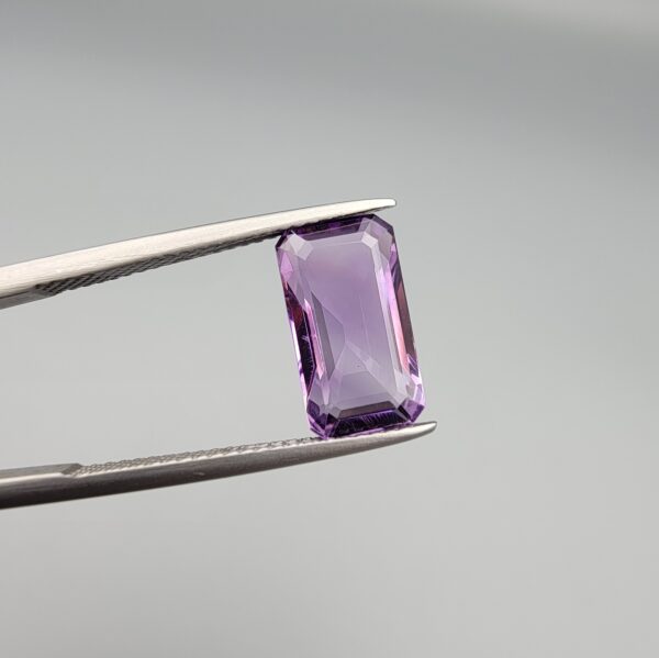 ​A natural 3.72-carat Brazilian amethyst (Katela) with a bright purple saturation and a sharp rectangle faceted cut, held in professional jeweler's tweezers.