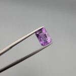 A natural 2.34-carat Brazilian amethyst (Katela) with a bright purple saturation and a sharp rectangle faceted cut, held in professional jeweler's tweezers.
