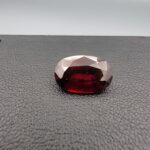 A natural 3.80-carat Red Garnet from Madagascar with a deep red sparkle and a polished oval faceted cut, resting on a black textured surface as shown in file 20260511_160015.jpg.