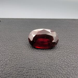 A natural 3.80-carat Red Garnet from Madagascar with a deep red sparkle and a polished oval faceted cut, resting on a black textured surface as shown in file 20260511_160015.jpg.