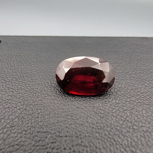 A natural 3.80-carat Red Garnet from Madagascar with a deep red sparkle and a polished oval faceted cut, resting on a black textured surface as shown in file 20260511_160015.jpg.