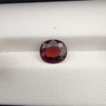 A natural 2.14-carat Red Garnet from Madagascar with a deep red sparkle and a polished oval faceted cut, resting on a white textured surface as shown in file 20260512_205905.jpg.