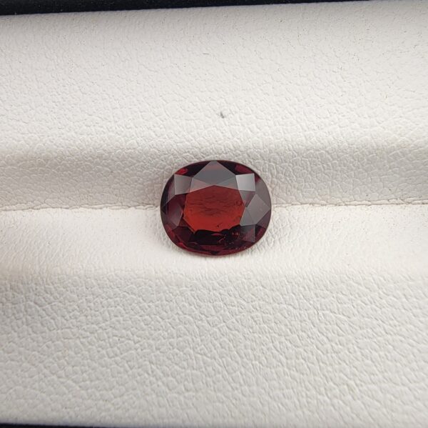 A natural 2.14-carat Red Garnet from Madagascar with a deep red sparkle and a polished oval faceted cut, resting on a white textured surface as shown in file 20260512_205905.jpg.