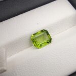 A natural 2.04-carat bright olive-green peridot (Zabarjad) from Kohistan, Pakistan, featuring a faceted oval cut, held securely in professional jeweler's tweezers.