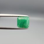 A natural 2.85-carat green emerald from the Swat Valley, Pakistan, featuring an octagon step cut and soft green saturation, held in professional jeweler's tweezers.
