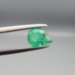 ​A natural 0.88-carat green emerald from the Swat Valley, Pakistan, featuring a faceted pear cut and vivid saturation, held in professional jeweler's tweezers.