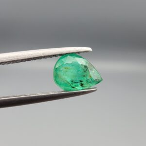 ​A natural 0.88-carat green emerald from the Swat Valley, Pakistan, featuring a faceted pear cut and vivid saturation, held in professional jeweler's tweezers.