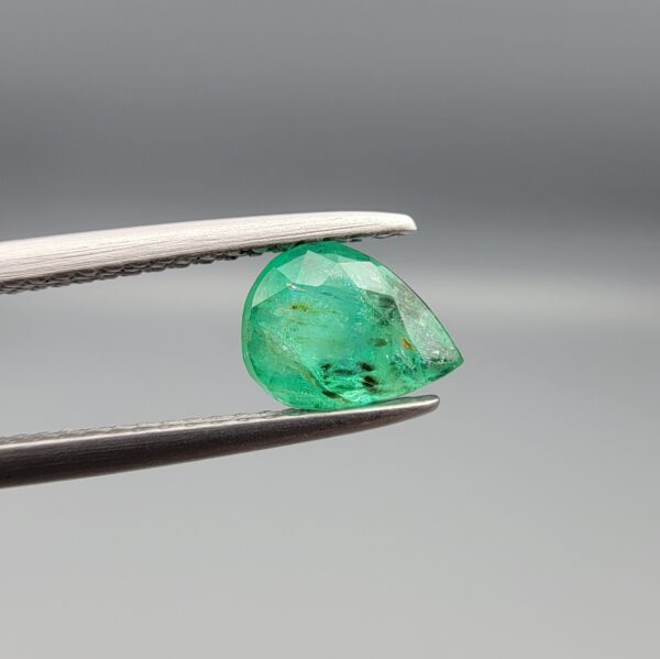 ​A natural 0.88-carat green emerald from the Swat Valley, Pakistan, featuring a faceted pear cut and vivid saturation, held in professional jeweler's tweezers.