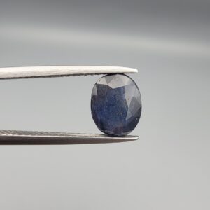 A natural 2.85-carat blue sapphire (Neelam) from Madagascar, featuring a deep navy blue hue and a masterfully faceted oval cut, held in professional jeweler's tweezers.