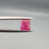 ​A natural 1.09-carat pinkish-red ruby from Mozambique featuring an octagon step cut with unique internal crystal inclusions, held in professional jeweler's tweezers.