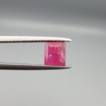 ​A natural 1.09-carat pinkish-red ruby from Mozambique featuring an octagon step cut with unique internal crystal inclusions, held in professional jeweler's tweezers.