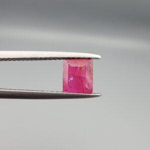 ​A natural 1.09-carat pinkish-red ruby from Mozambique featuring an octagon step cut with unique internal crystal inclusions, held in professional jeweler's tweezers.