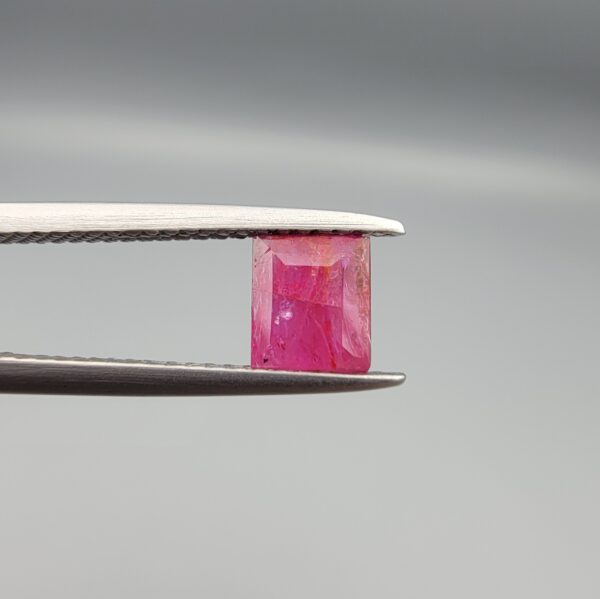 ​A natural 1.09-carat pinkish-red ruby from Mozambique featuring an octagon step cut with unique internal crystal inclusions, held in professional jeweler's tweezers.