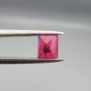 ​A natural 1.09-carat pinkish-red ruby from Mozambique featuring an octagon step cut with unique internal crystal inclusions, held in professional jeweler's tweezers.