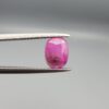 ​A natural 1.21-carat pinkish-red ruby from Mozambique featuring a faceted oval cut with a distinct dark natural inclusion, held in professional jeweler's tweezers.