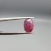 ​A natural 1.85-carat pinkish-red ruby from Mozambique featuring a faceted oval cut with visible natural internal silk and crystal inclusions, held in professional jeweler's tweezers.