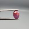 ​A natural 1.85-carat pinkish-red ruby from Mozambique featuring a faceted oval cut with visible natural internal silk and crystal inclusions, held in professional jeweler's tweezers.
