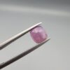 ​A natural 0.97-carat pinkish-red ruby from Mozambique featuring a faceted oval cut with visible natural internal birthmarks and silky inclusions, held in professional jeweler's tweezers.